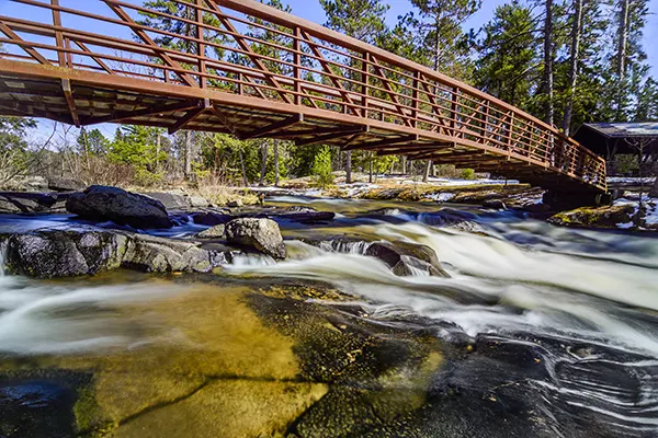A bridge spans the waterfall along the trail at Rushing River Provincial Park.