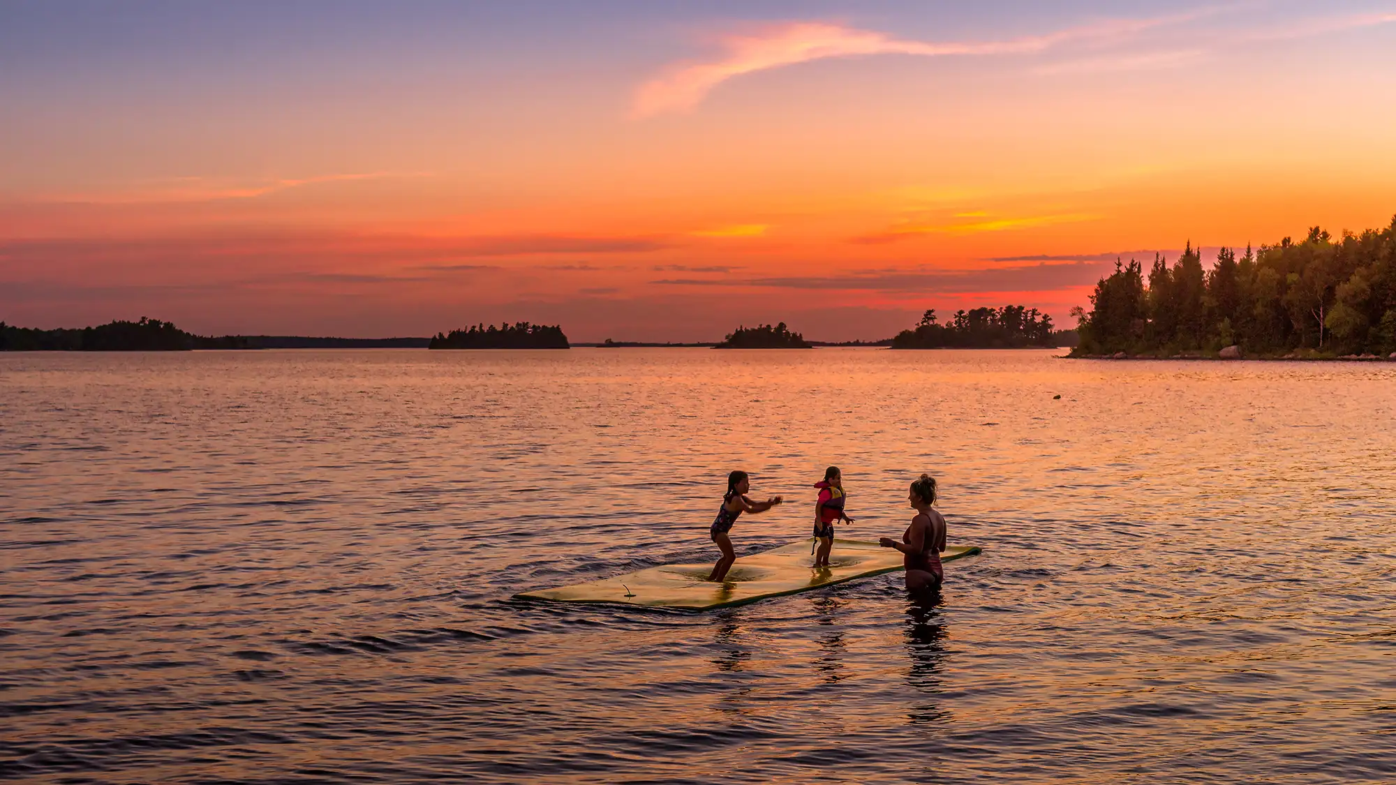 A mother and two girls swimming at sunset.